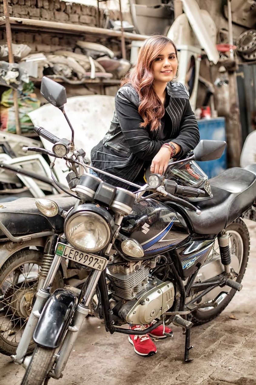 En ung kvinde i læderjakke sidder selvsikkert på en klassisk motorcykel i et værksted.